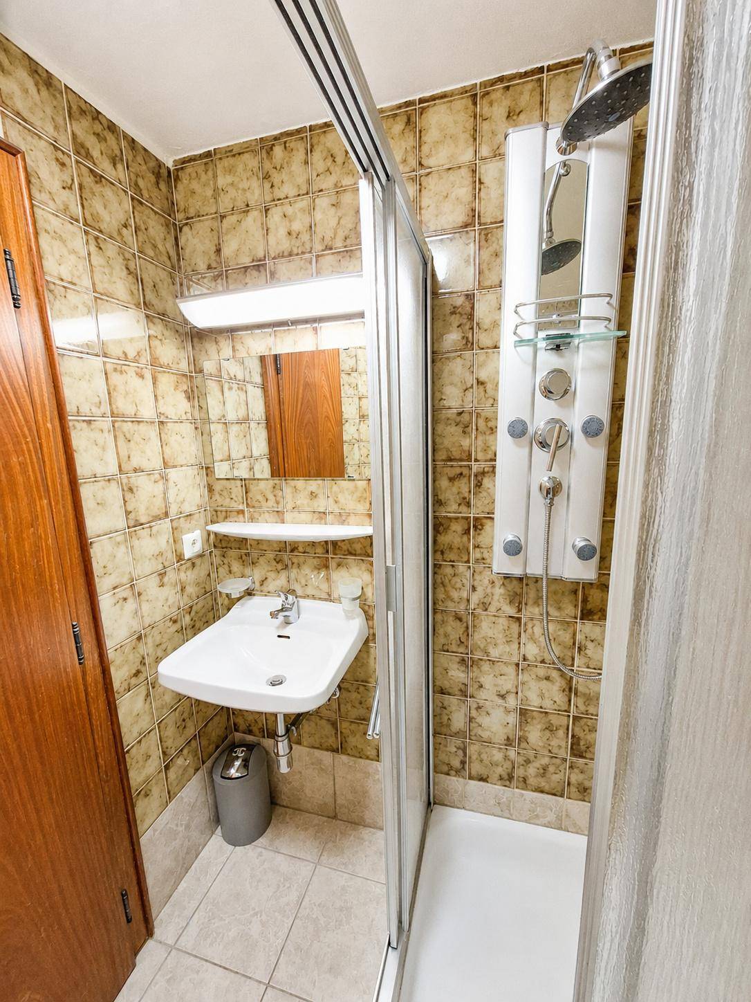 Kleines Badezimmer mit braunen Fliesen, Waschbecken und einer Duschkabine mit Massagedüsen.