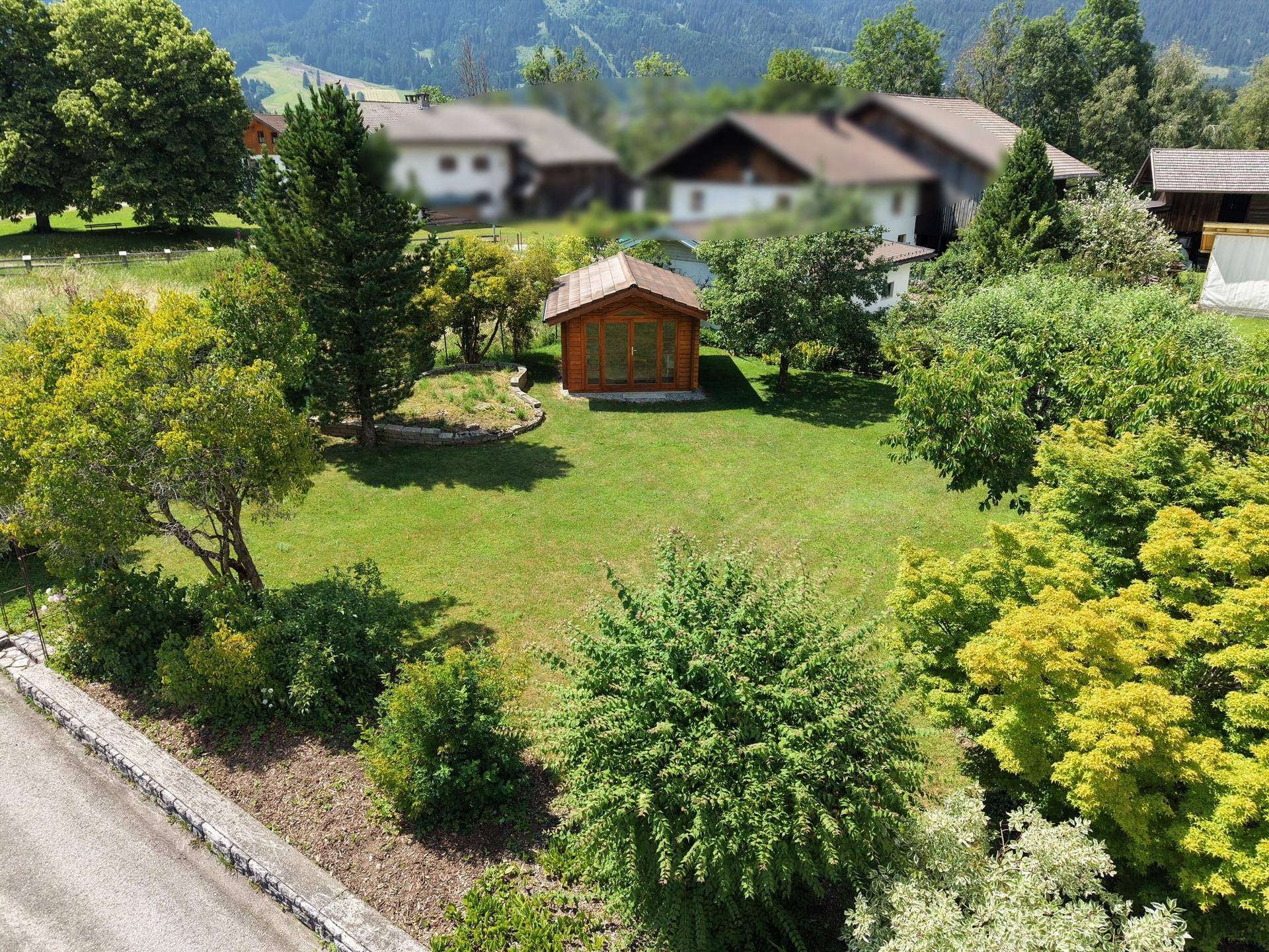 Großer, gepflegter Garten mit Rasenfläche und einem charmanten Holzgartenhaus unter blauem Himmel.