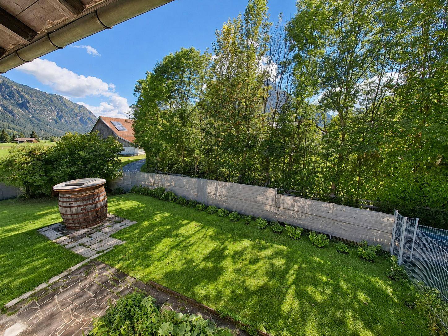 Grüner Gartenbereich mit Rasenfläche und einem dekorativen Holzfass, umgeben von Natur.