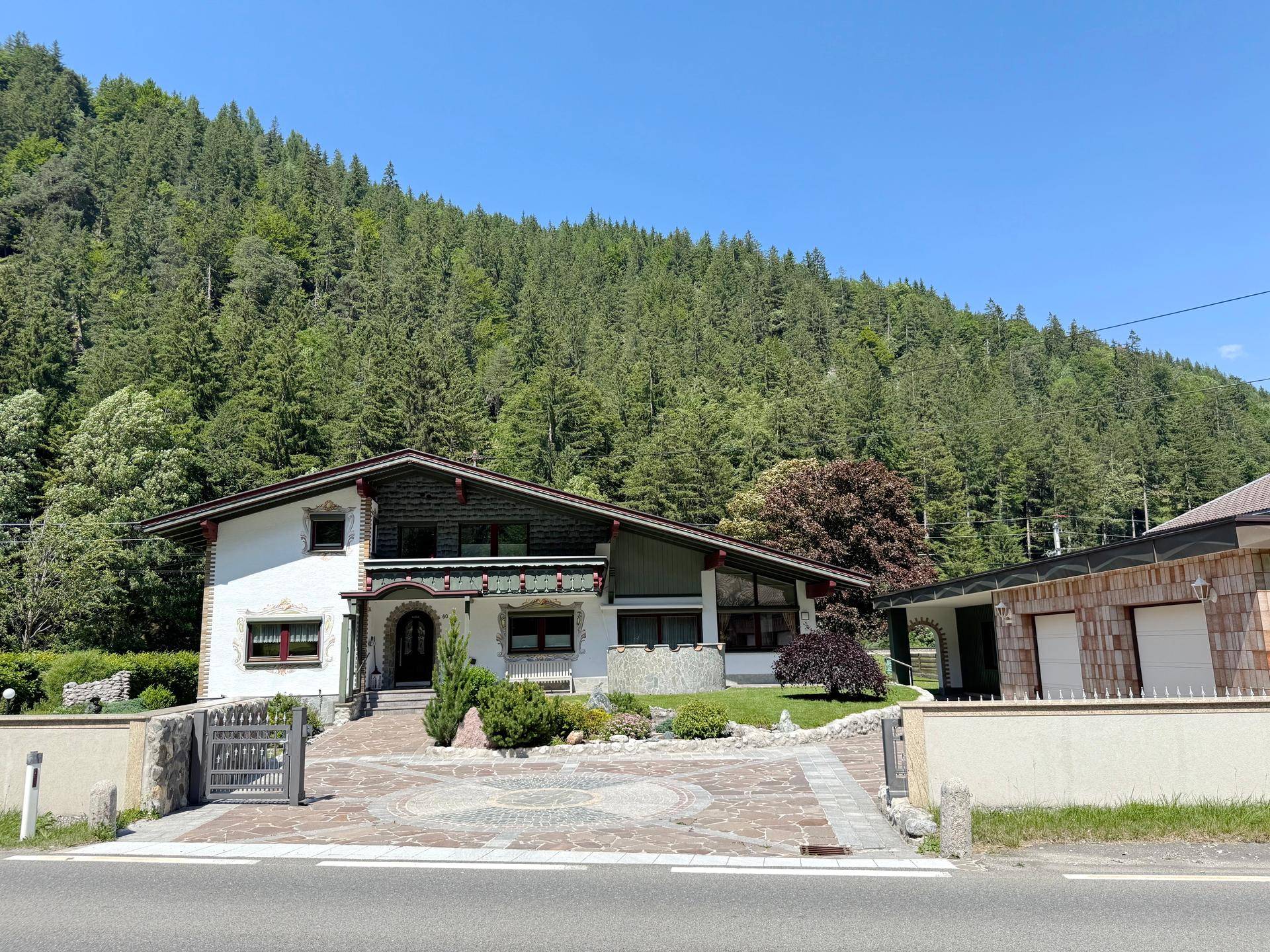 Gesamtansicht des Alpenhauses von der Straße, umgeben von Natur und einem separaten Garagengebäude.