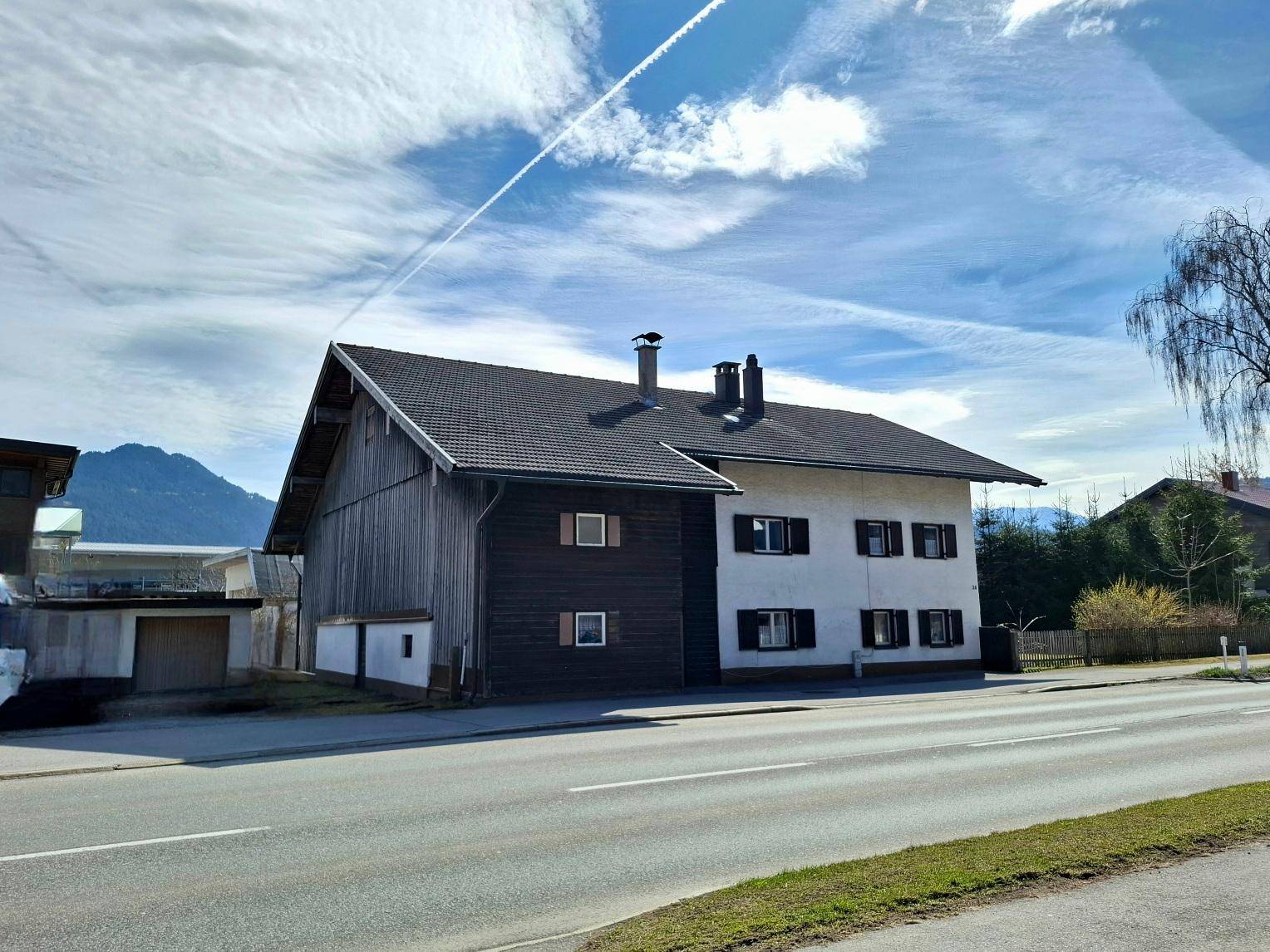 Haus mit traditioneller Architektur, weißer Fassade und dunkler Holzverkleidung an der Giebelseite.