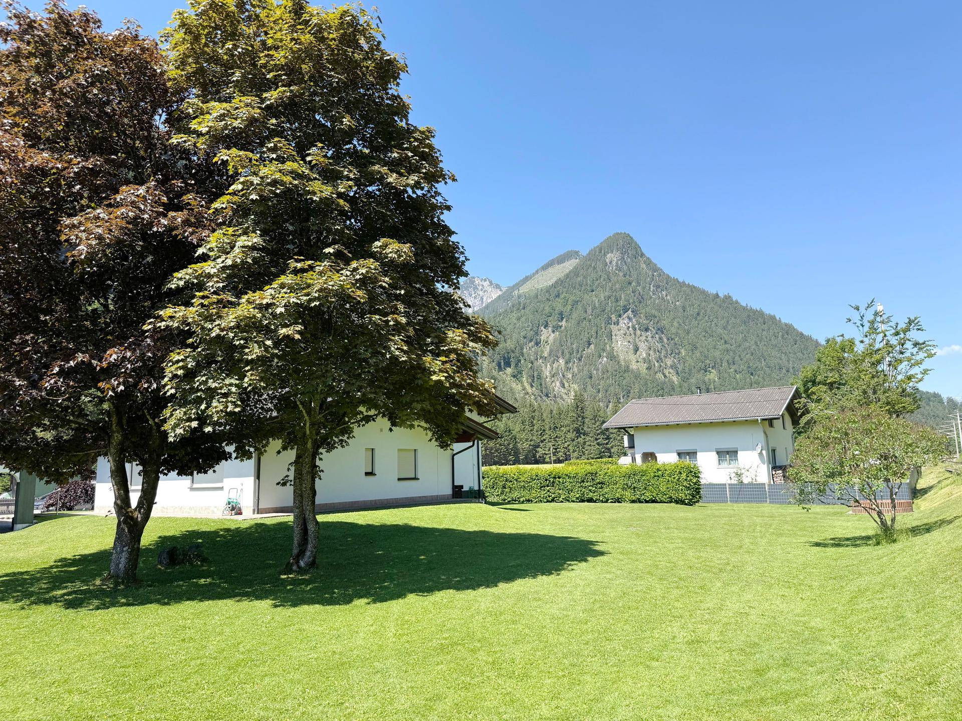 Weitläufiger Gartenbereich mit großen Bäumen, gepflegtem Rasen und beeindruckendem Bergblick.