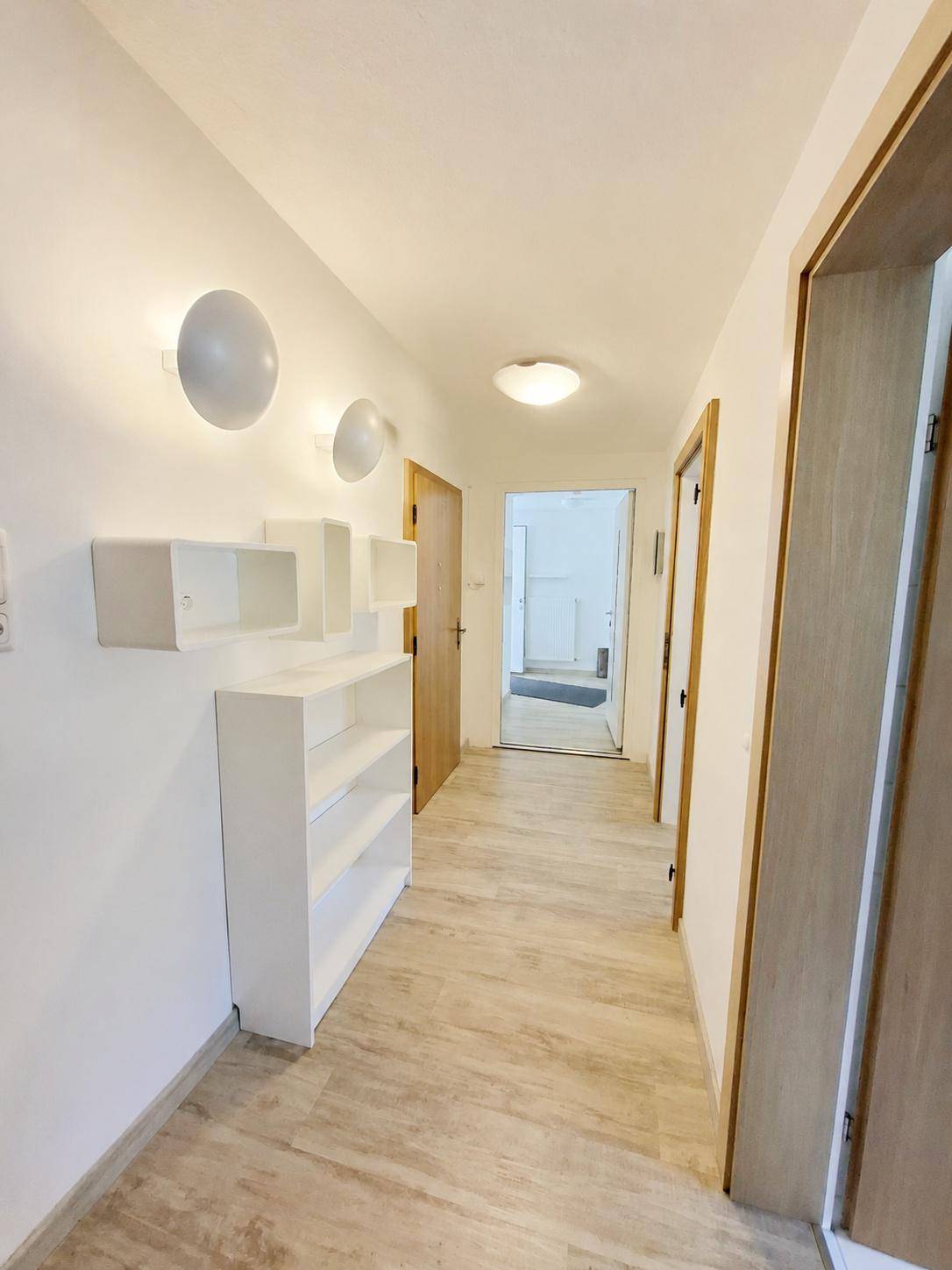 Langer, heller Flur mit Holzfußboden, weißen Wänden und praktischen Regalelementen.