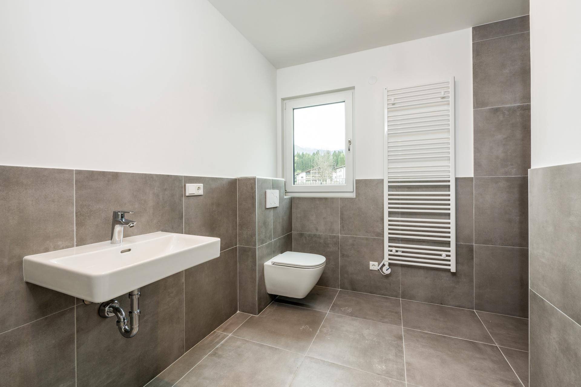 Modernes Badezimmer mit grauen Fliesen, wandhängendem WC und Waschbecken.