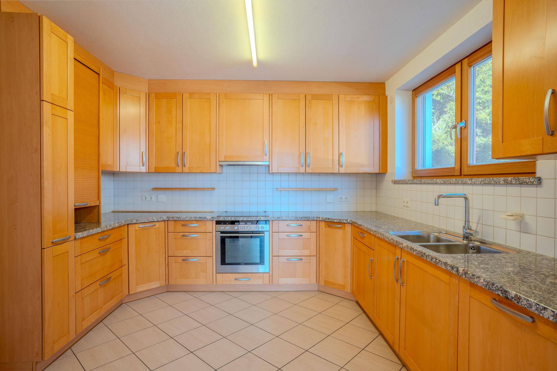Funktionale Küche mit hellen Holzschränken, Granitarbeitsplatten, Fliesenrückwand und einem Fenster.