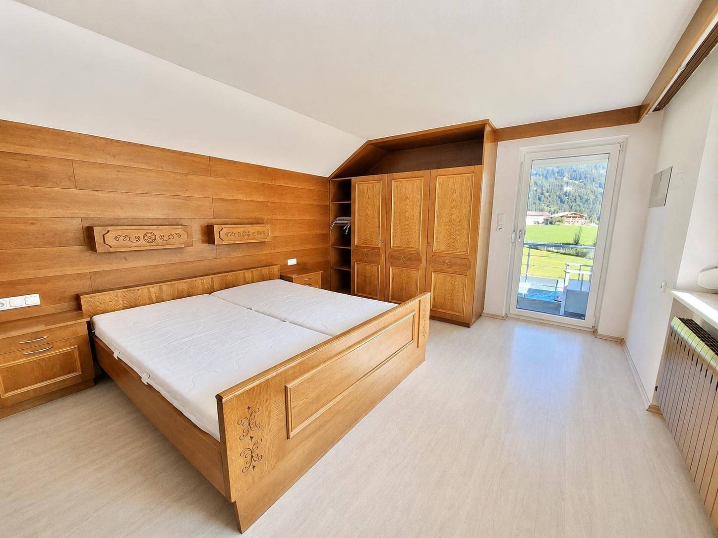 Helles Schlafzimmer mit Holzeinrichtung, Fenster und Zugang zu einem Außenbereich.