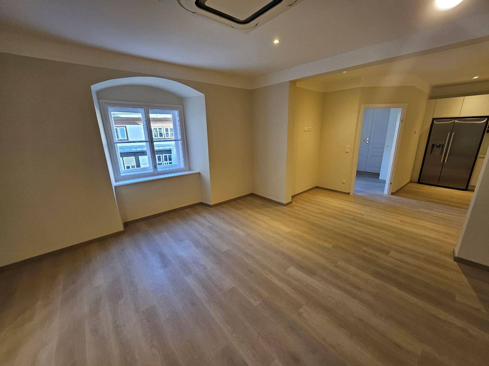 Heller Wohnraum mit Laminatboden und Blick auf den angrenzenden Küchenbereich mit Kühlschrank.