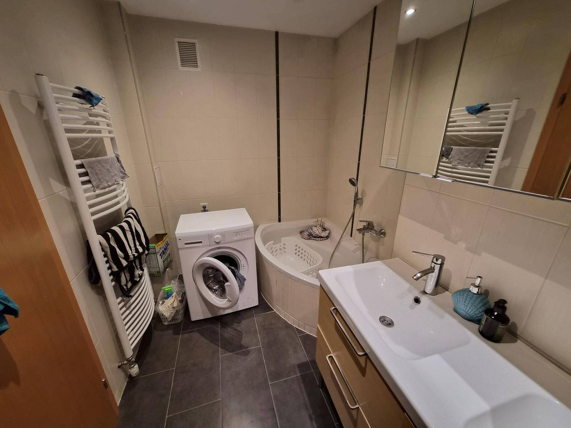 Badezimmer mit Eckbadewanne, Waschmaschine, Einzelwaschbecken und Handtuchheizkörper.