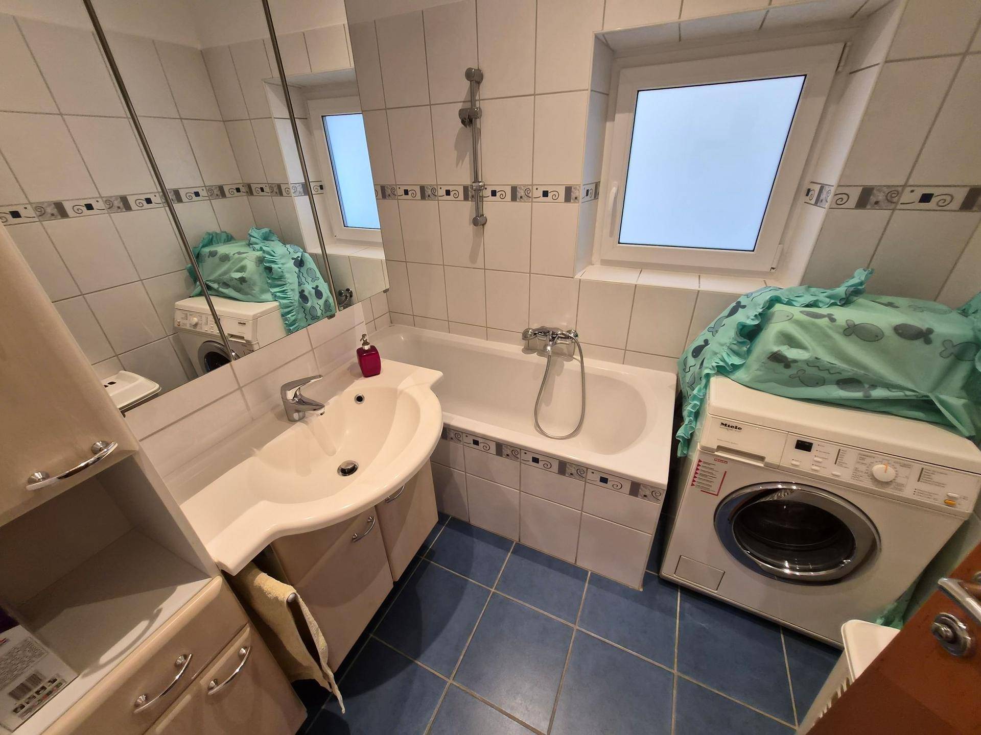 Badezimmer mit Badewanne, Waschbecken, Spiegel und einer Waschmaschine.