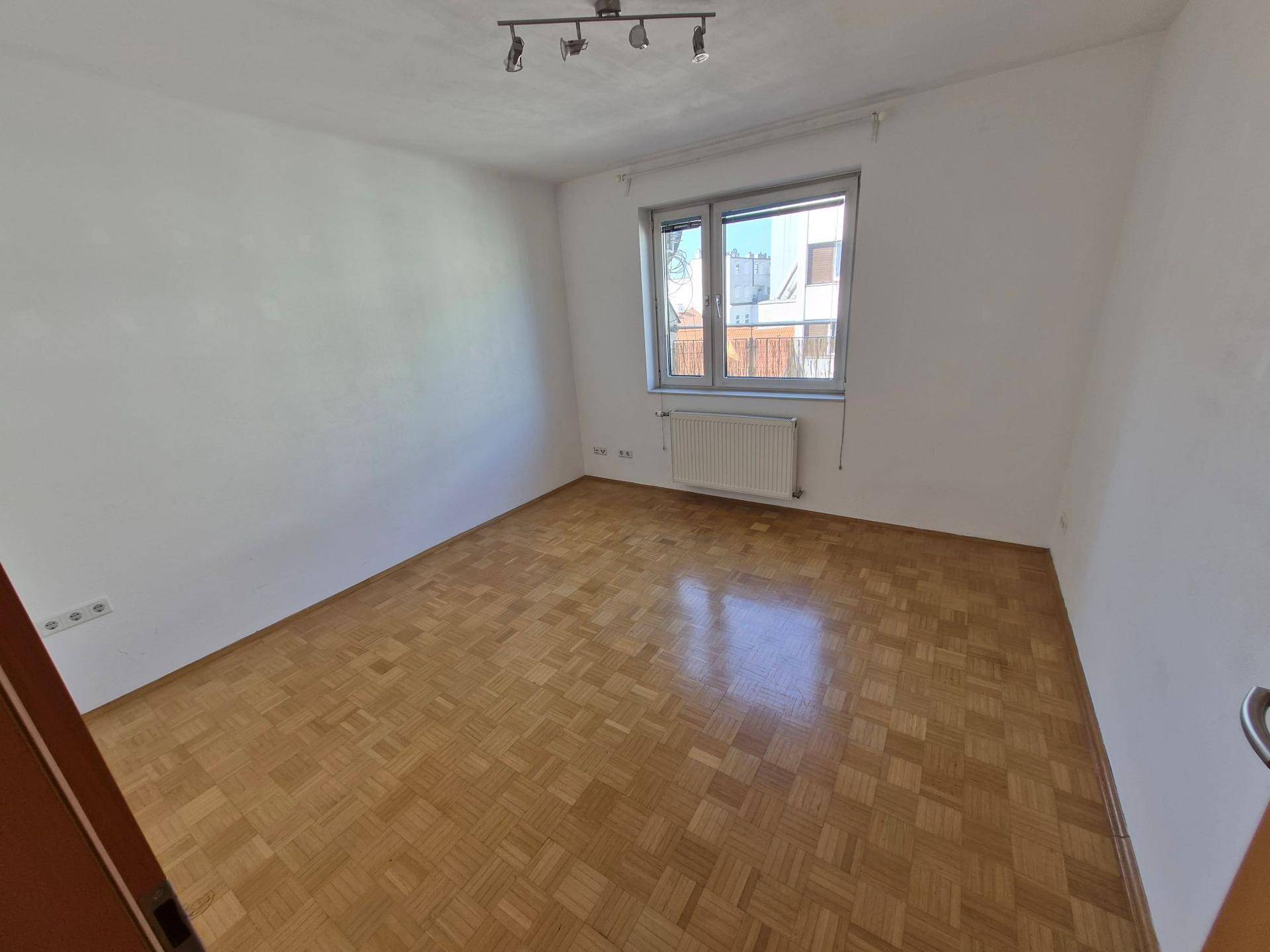 Leeres Schlafzimmer mit hellem Parkettboden, weißen Wänden und einem Fenster.