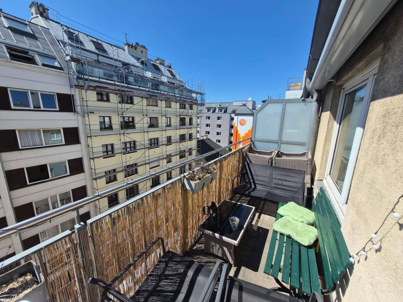 Balkon mit Outdoor-Möbeln, Bambusverkleidung und Blick auf die umliegenden Gebäude.