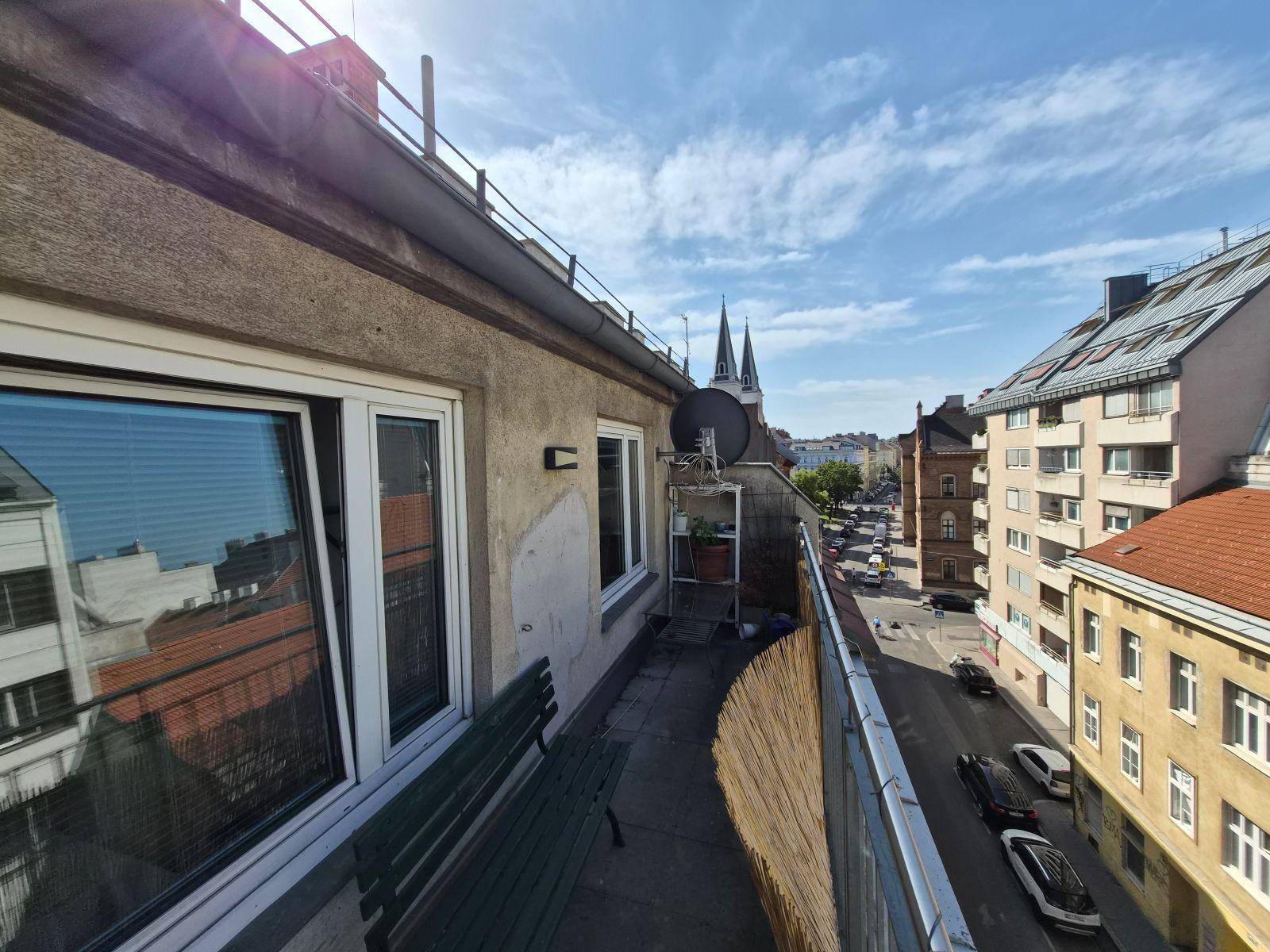 Langer Balkon mit Sitzbank, Bambusverkleidung und Blick auf die Straße und Kirchtürme.