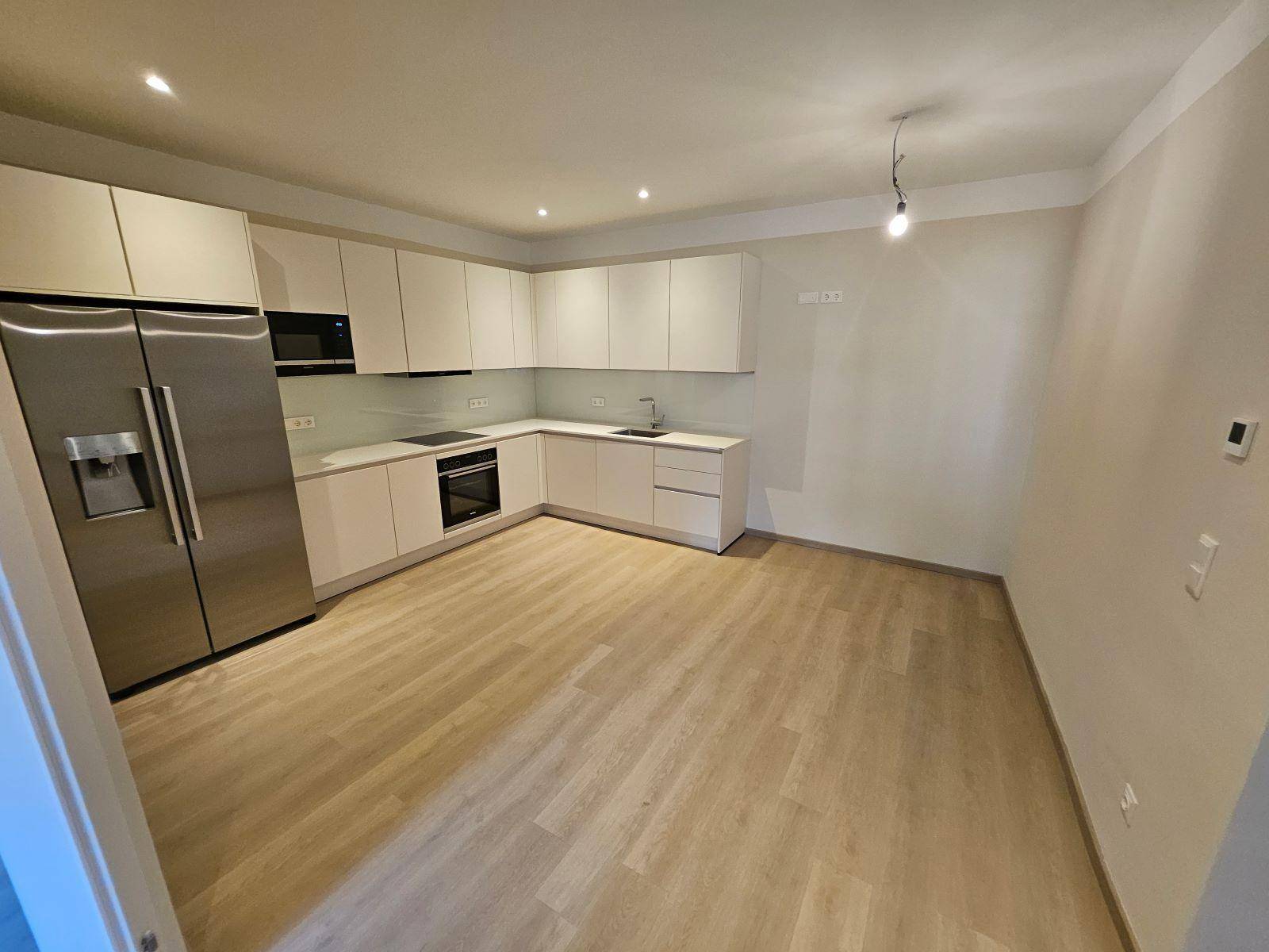 Moderne Einbauküche mit weißen Schränken, Edelstahlgeräten und hellem Laminatboden.