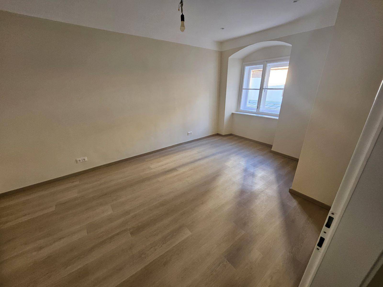 Ruhiges Schlafzimmer mit hellem Laminatboden und einem Fenster für natürliches Licht.