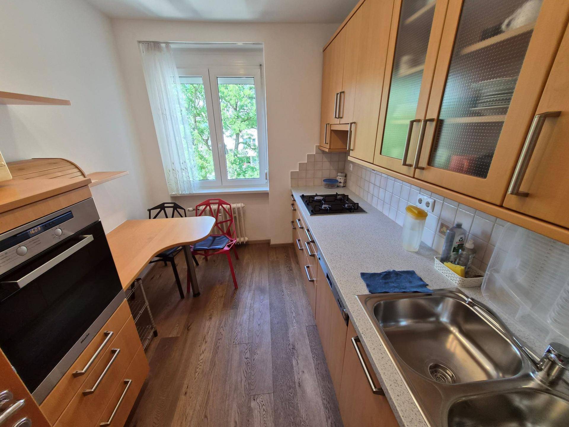 Funktionale Küche mit Holzschränken, Gasherd, Backofen und einem kleinen Essbereich am Fenster.