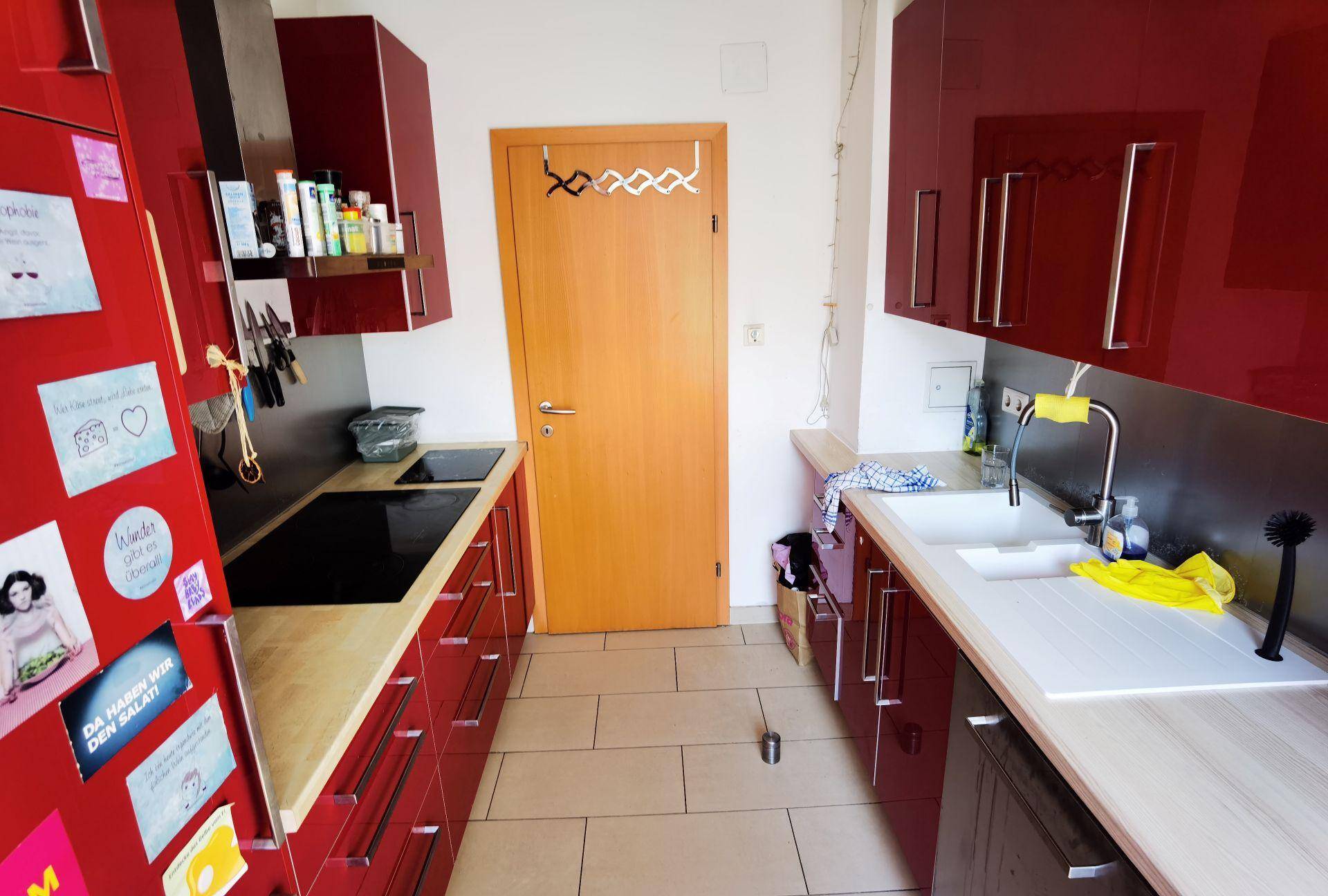 Funktionale Küche mit roten Schränken, Induktionskochfeld und Spülbereich.