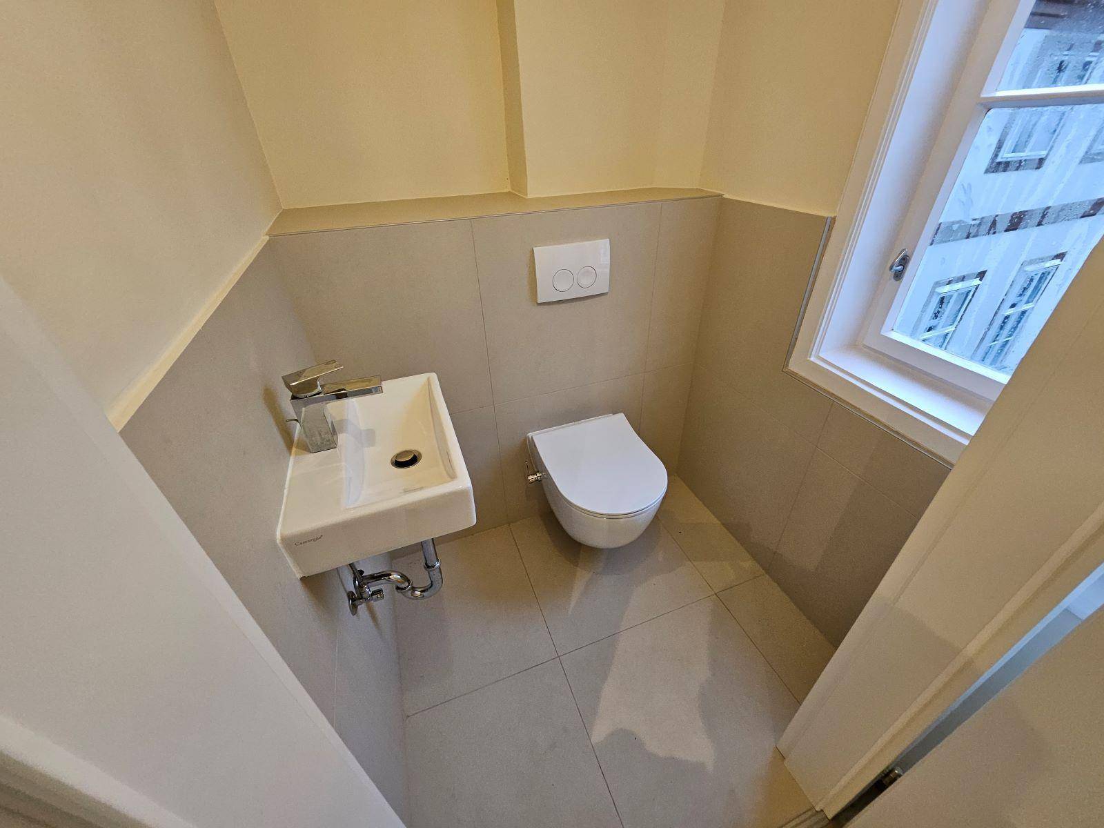 Kleines Gäste-WC mit wandhängender Toilette, Waschbecken und Fenster für Belüftung.