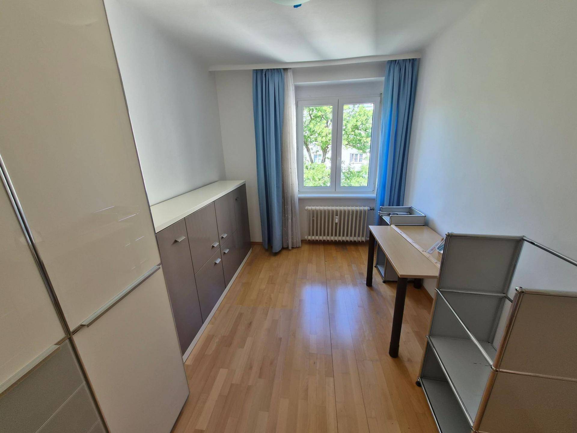 Freundliches Arbeitszimmer mit Holzfußboden, langen Schränken und einem Schreibtisch am Fenster.