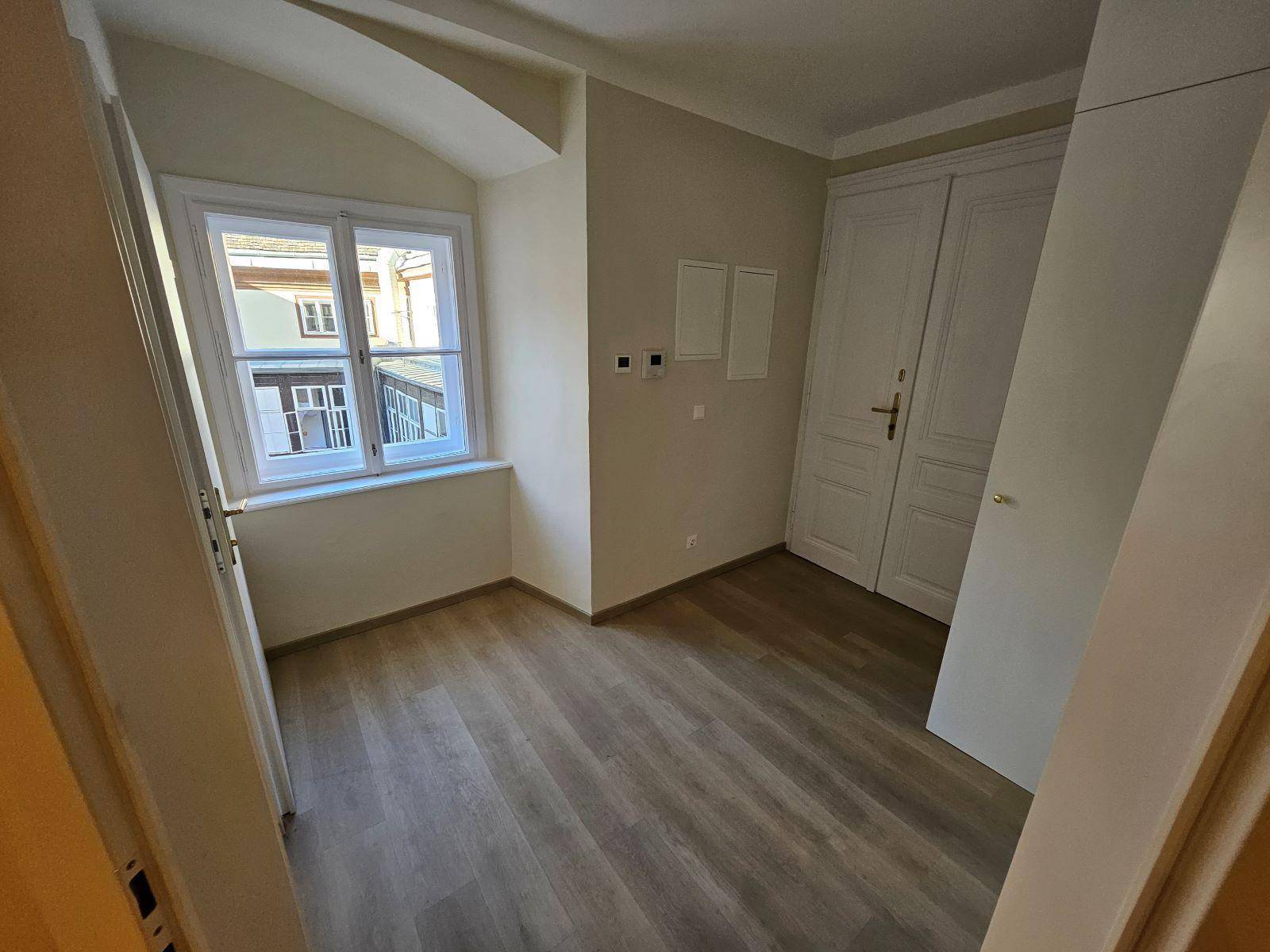 Gemütliches Zimmer mit Laminatboden, Fenster und praktischen weißen Einbauschränken.