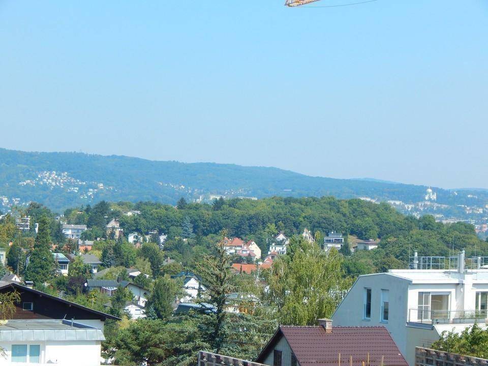 Panoramablick über eine bewaldete Hügellandschaft mit Wohngebäuden und klarem Himmel.