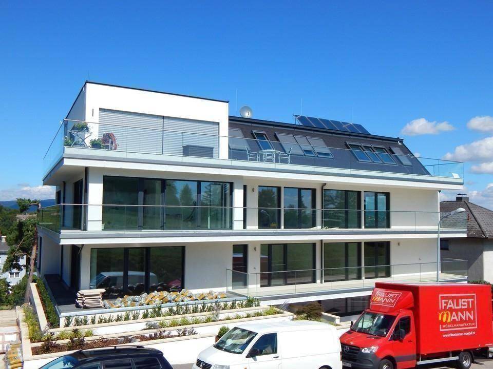 Modernes Wohngebäude mit mehreren Balkonen, großen Glasflächen und Solarpaneelen auf dem Dach.