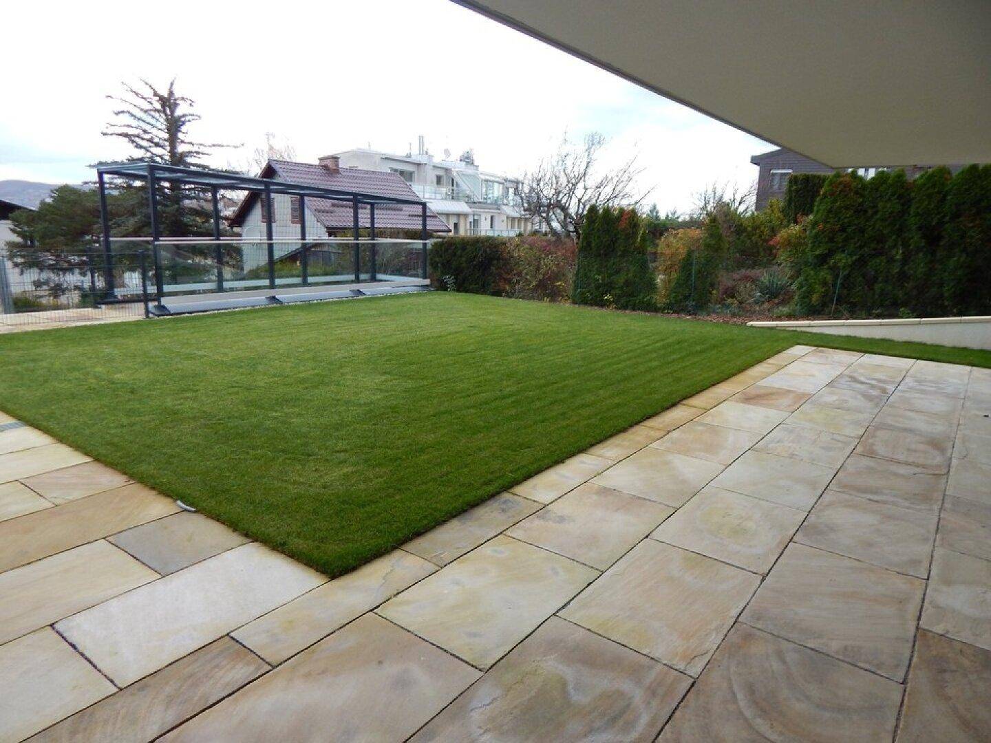 Gepflegter Gartenbereich mit Rasenfläche und großer gefliester Terrasse vor dem Gebäude.