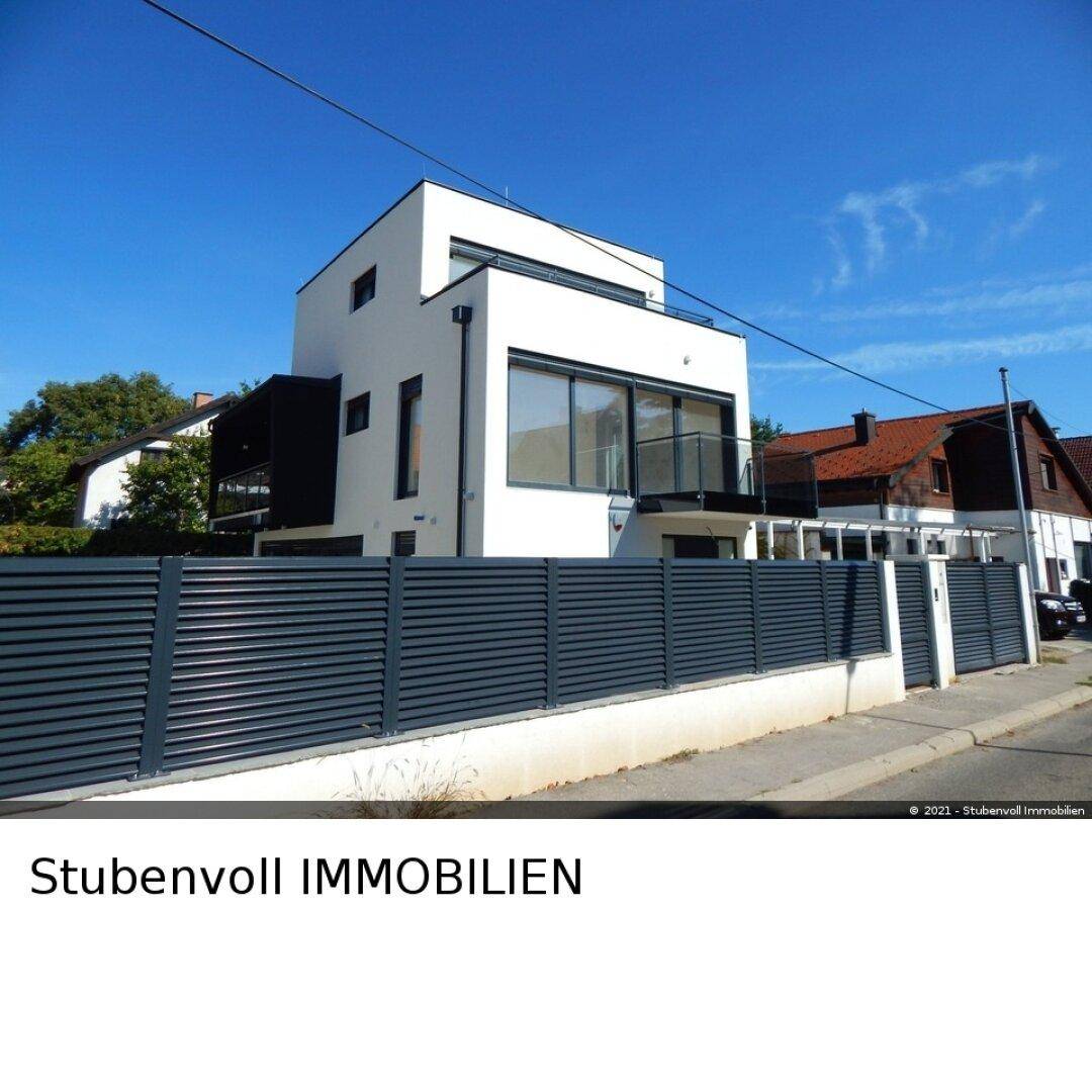 Modernes Wohnhaus mit weißer Fassade und dunklem Zaun, gesehen von der Straße.