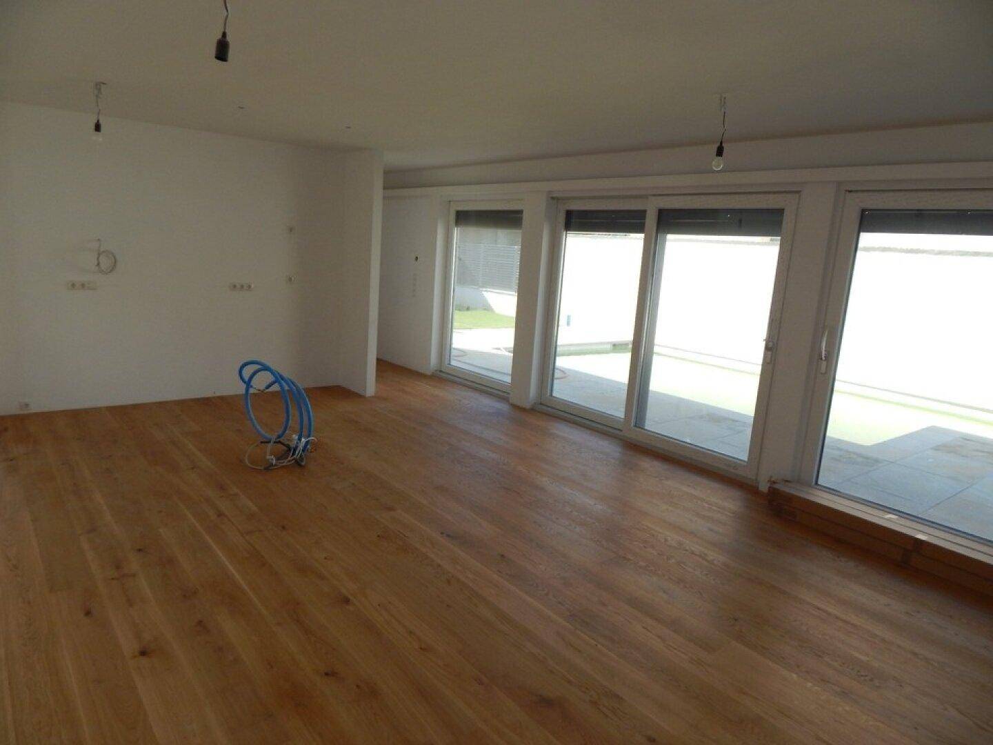 Großer, heller Wohnraum mit Eichenparkett und breiten Fensterfronten mit Rollläden.