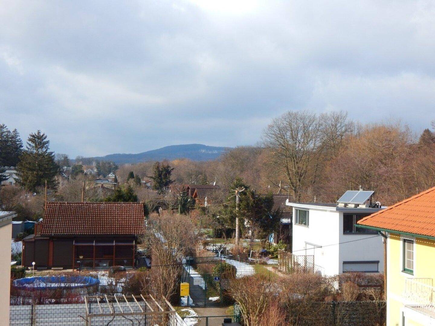 Weitläufiger Blick über die winterliche Landschaft mit Häusern und Bergen im Hintergrund.