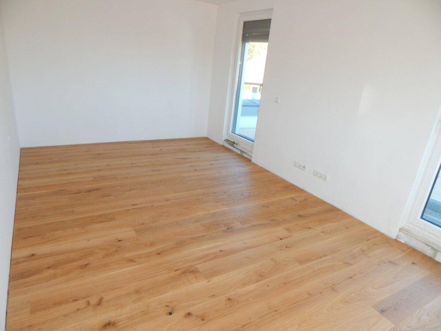Heller Raum mit Holzboden und zwei Zugängen zu einem Balkon, ideal für ein Schlafzimmer.