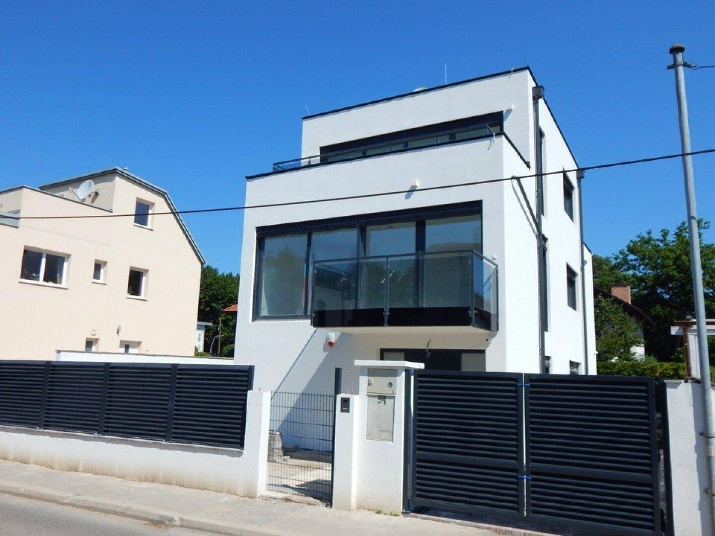 Elegante moderne Villa mit weißer Fassade, großen Fenstern und einem stilvollen Eingangstor.