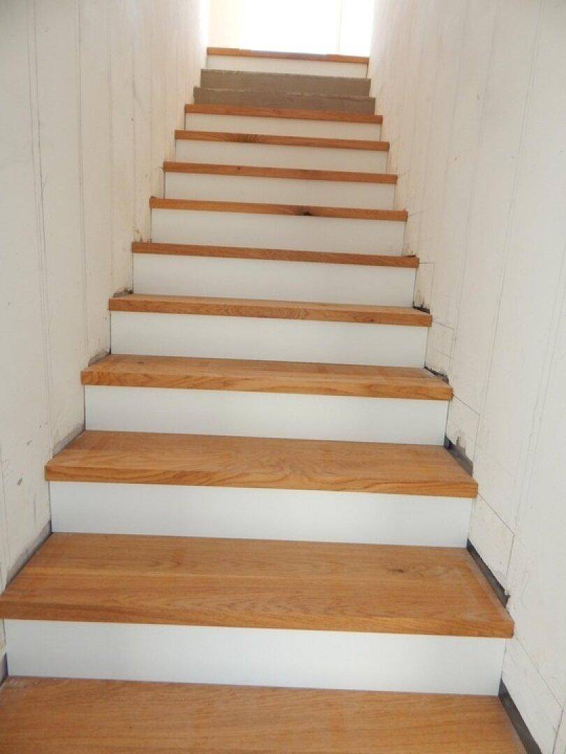 Treppe mit Holzstufen und weißen Setzstufen in einem noch unfertigen Innenbereich.