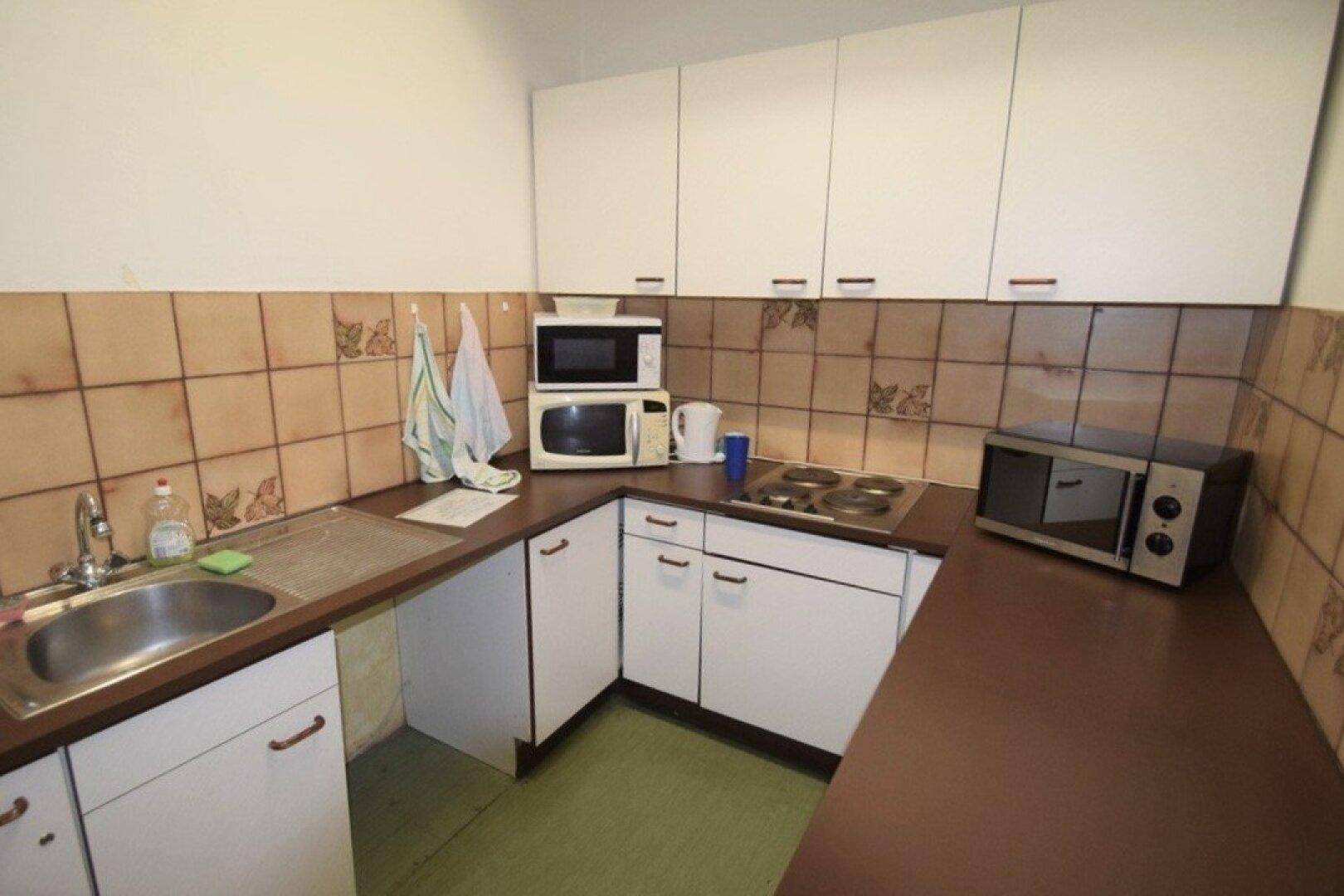 Kleine Küche mit weißen Oberschränken, braunen Arbeitsplatten und integrierten Elektrogeräten, mit Fliesenspiegel.