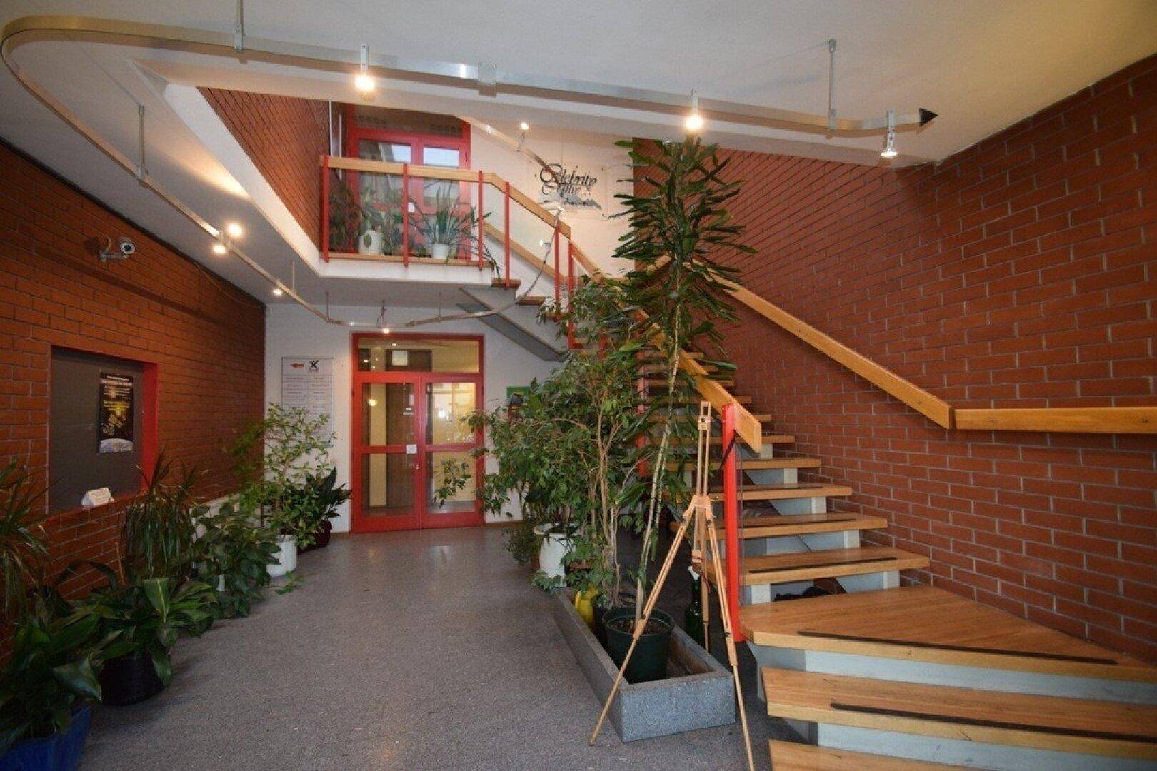 Heller Eingangsbereich mit Ziegelwänden, Holztreppe und vielen Pflanzen, einladend gestaltet.
