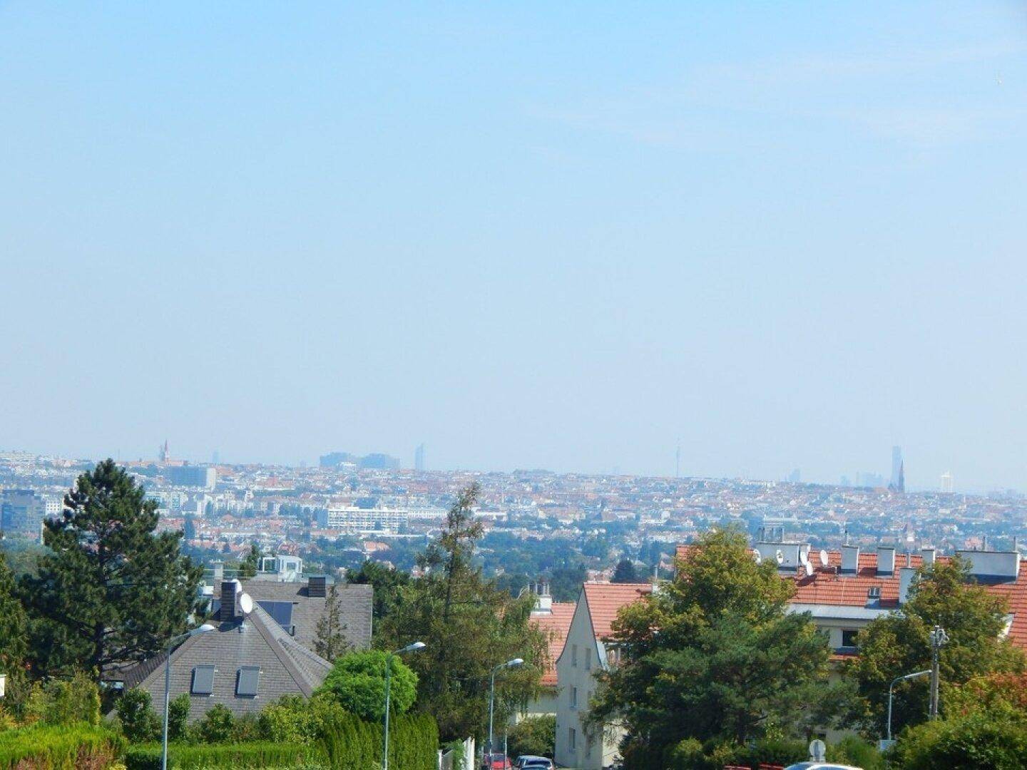 Weitläufiger Blick auf die Stadtkulisse mit Wohngebäuden und Bäumen im Vordergrund.