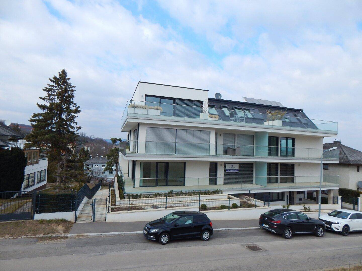 Modernes Wohngebäude mit mehreren Balkonen und Glasgeländern in städtischer Umgebung.