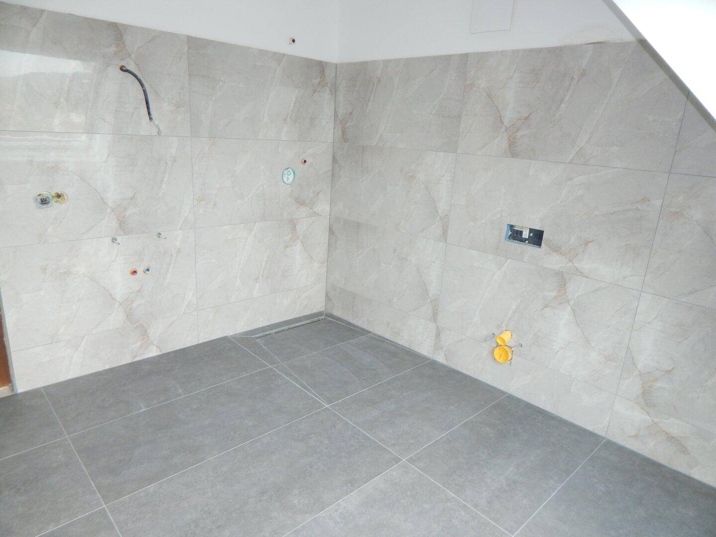 Unfertiges Badezimmer mit modernen grauen Boden- und Wandfliesen in Marmoroptik.