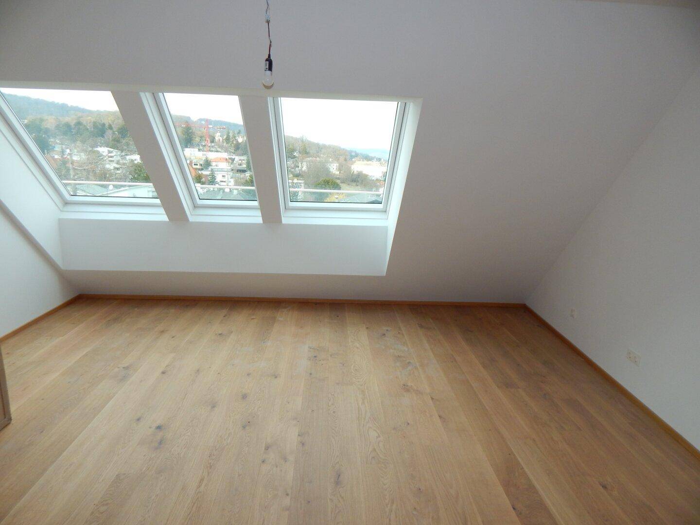 Dachgeschosszimmer mit Holzboden, schräger Decke und drei Dachfenstern mit Ausblick.