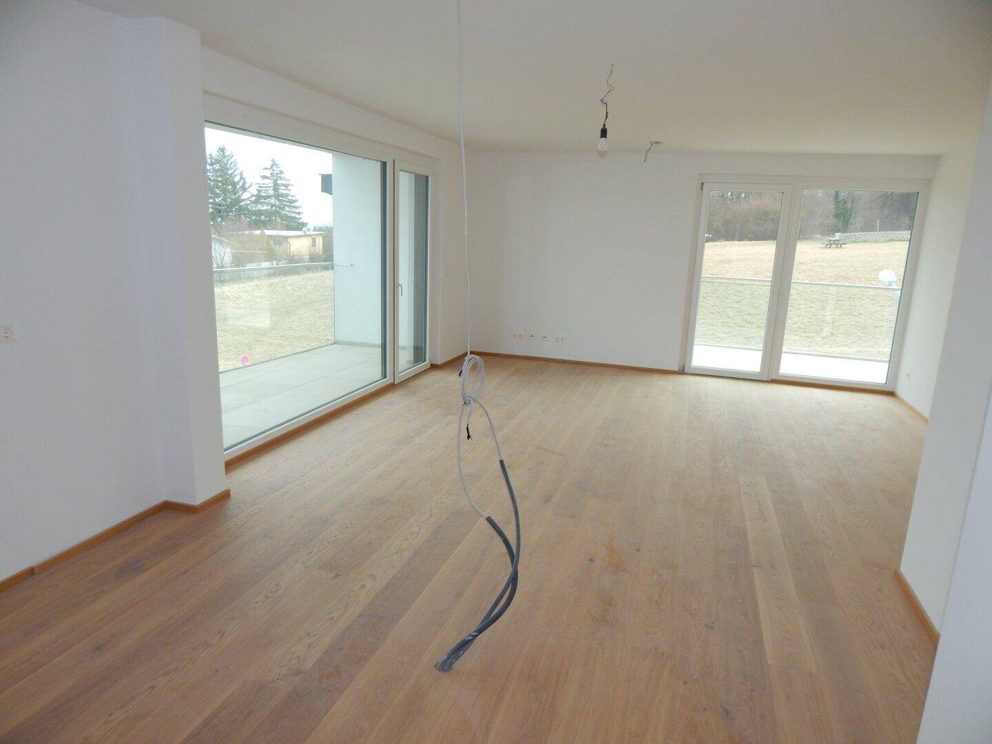 Geräumiger Wohnbereich mit Holzboden und Zugang zu einer Grünfläche im Freien.