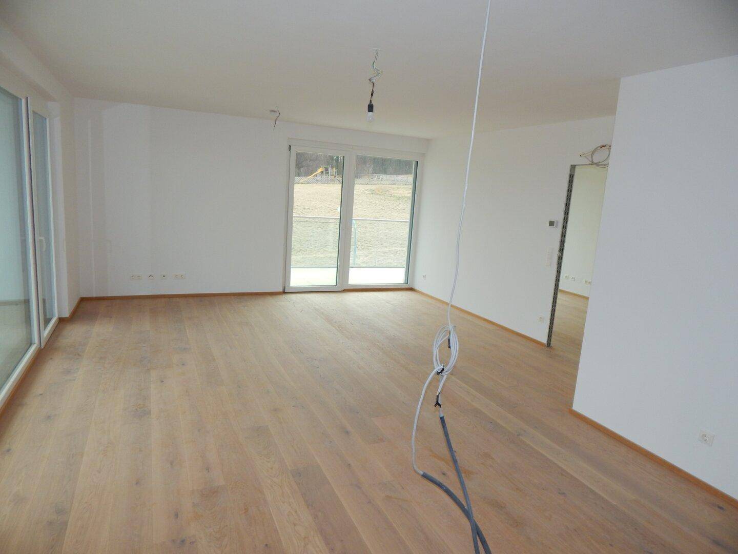 Heller Wohnraum mit Holzboden und großen Fenstern, die viel Tageslicht hereinlassen.
