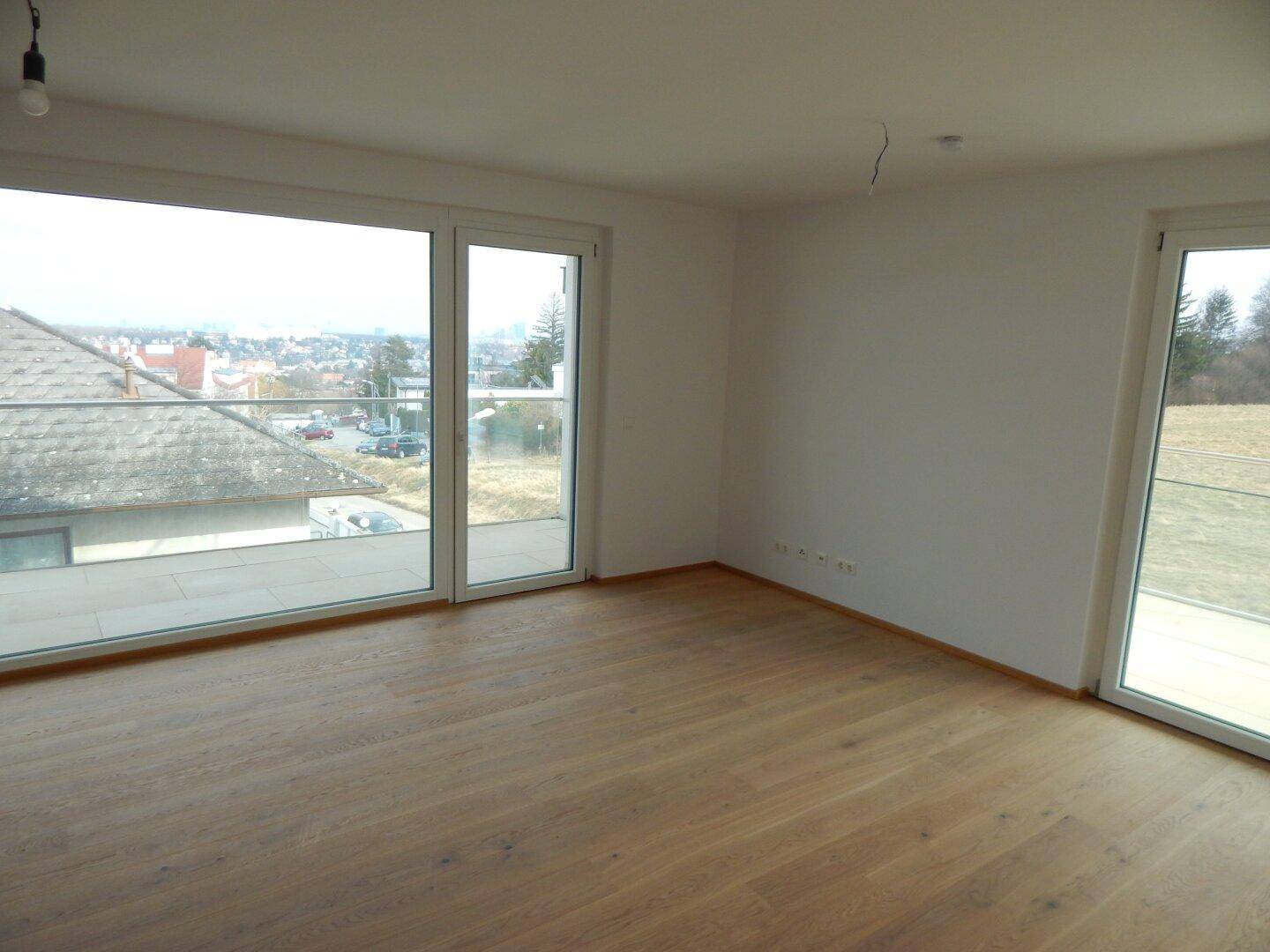 Heller Raum mit Holzboden und großen Schiebetüren, die auf eine Terrasse führen.