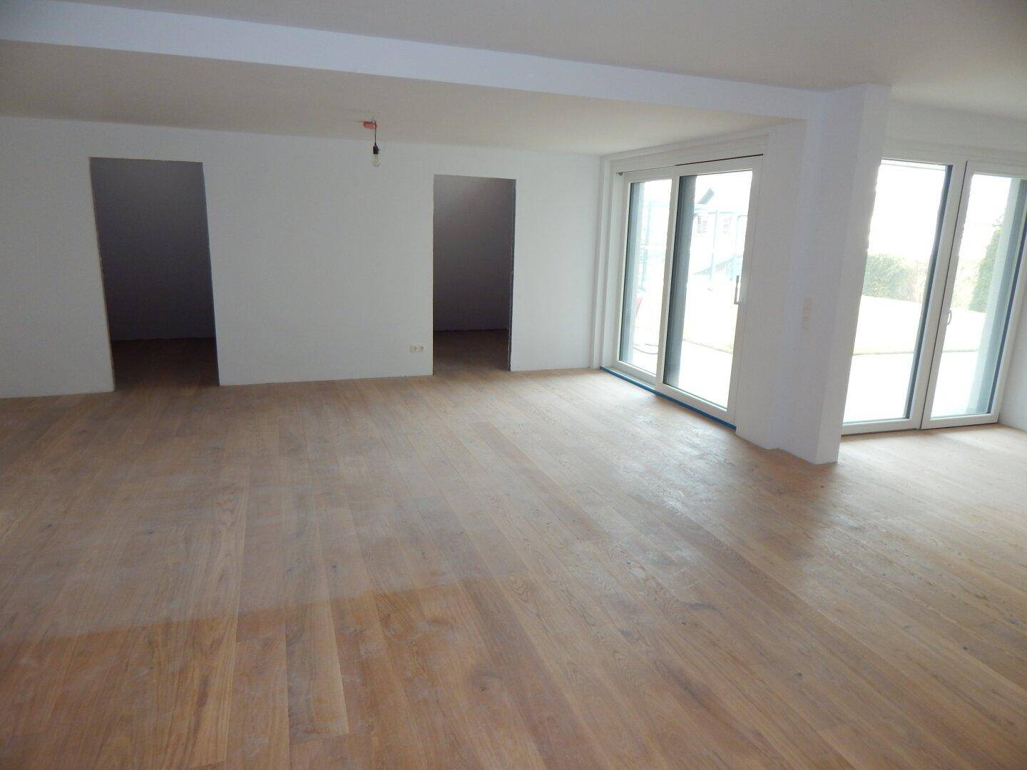 Geräumiger, unfertiger Wohnbereich mit Holzboden und großen Schiebetüren zum Außenbereich.