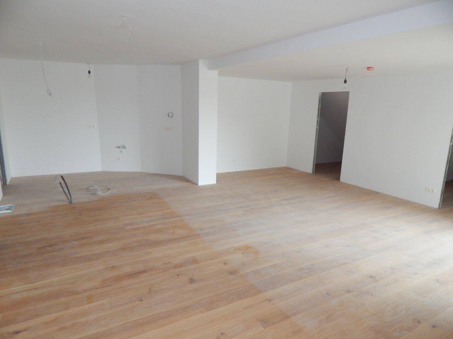 Heller, unfertiger Wohnraum mit Holzboden und vorbereiteten Anschlüssen für die Einrichtung.