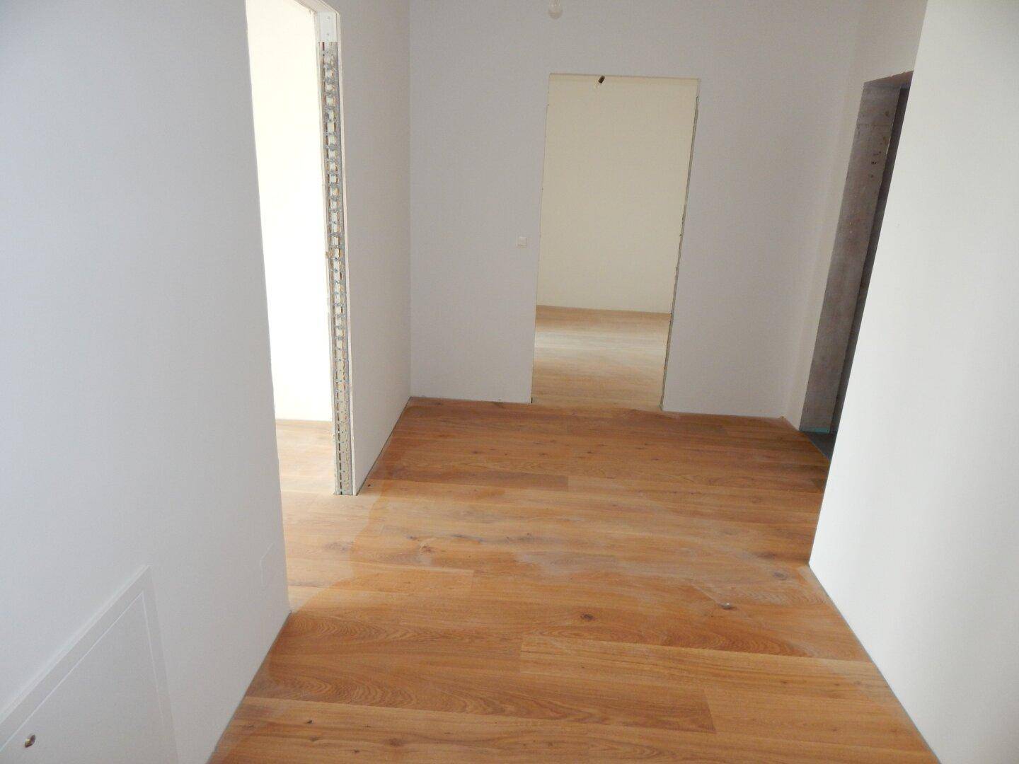Heller Flur mit Holzboden und offenen Türrahmen zu weiteren Räumen im Neubau.