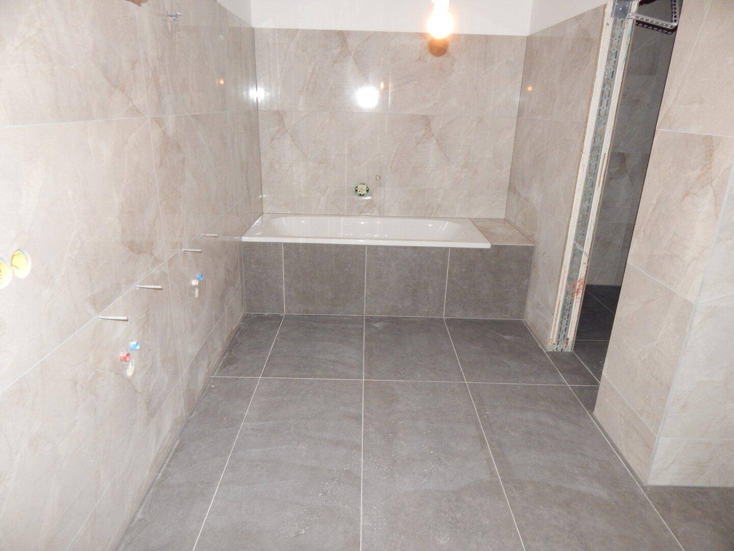 Unfertiges Badezimmer mit hellen Wandfliesen und dunkleren Bodenfliesen, bereit für Installationen.