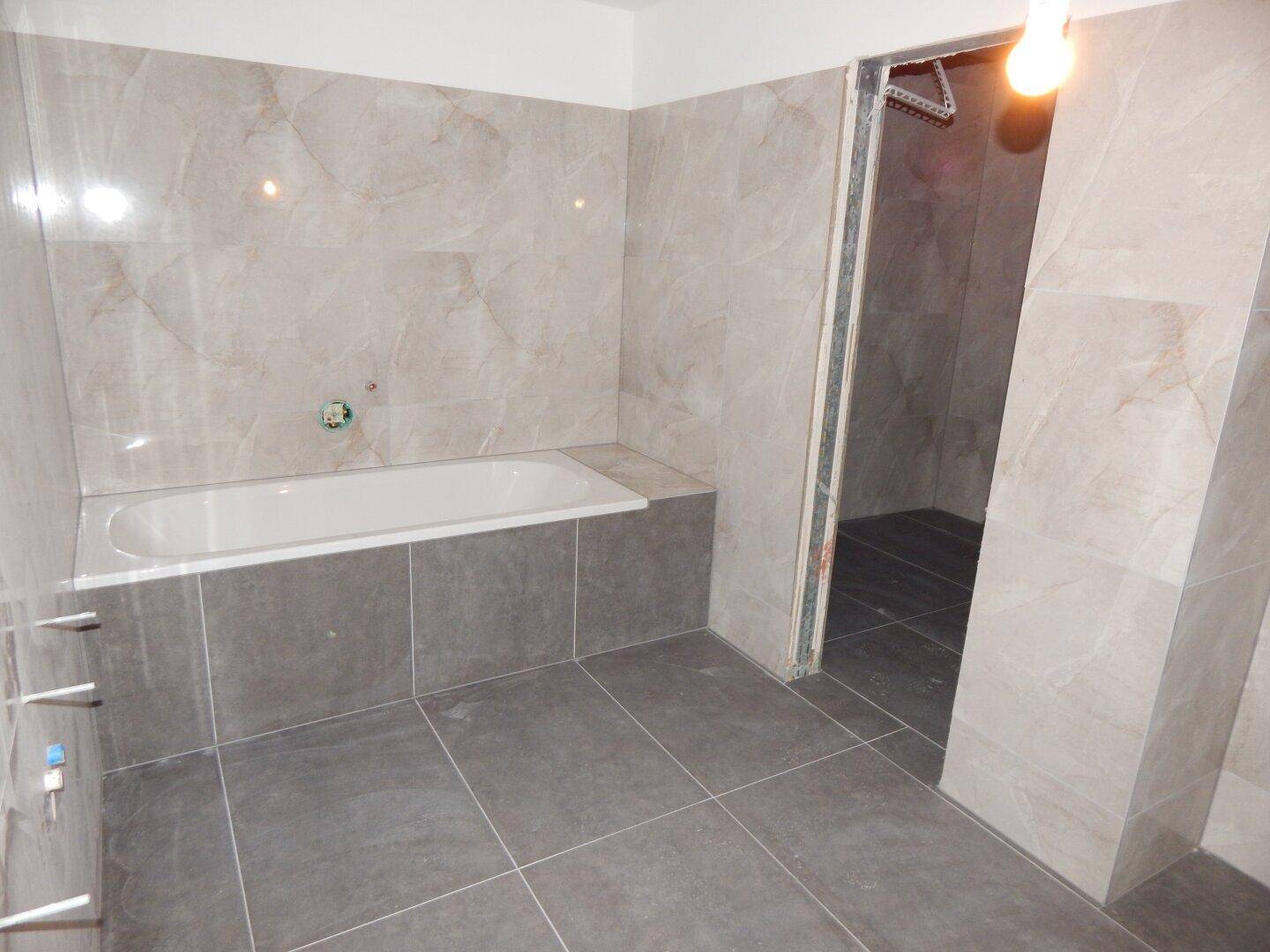Unfertiges Badezimmer mit eingebauter Badewanne und vorbereiteten Anschlüssen für Armaturen.