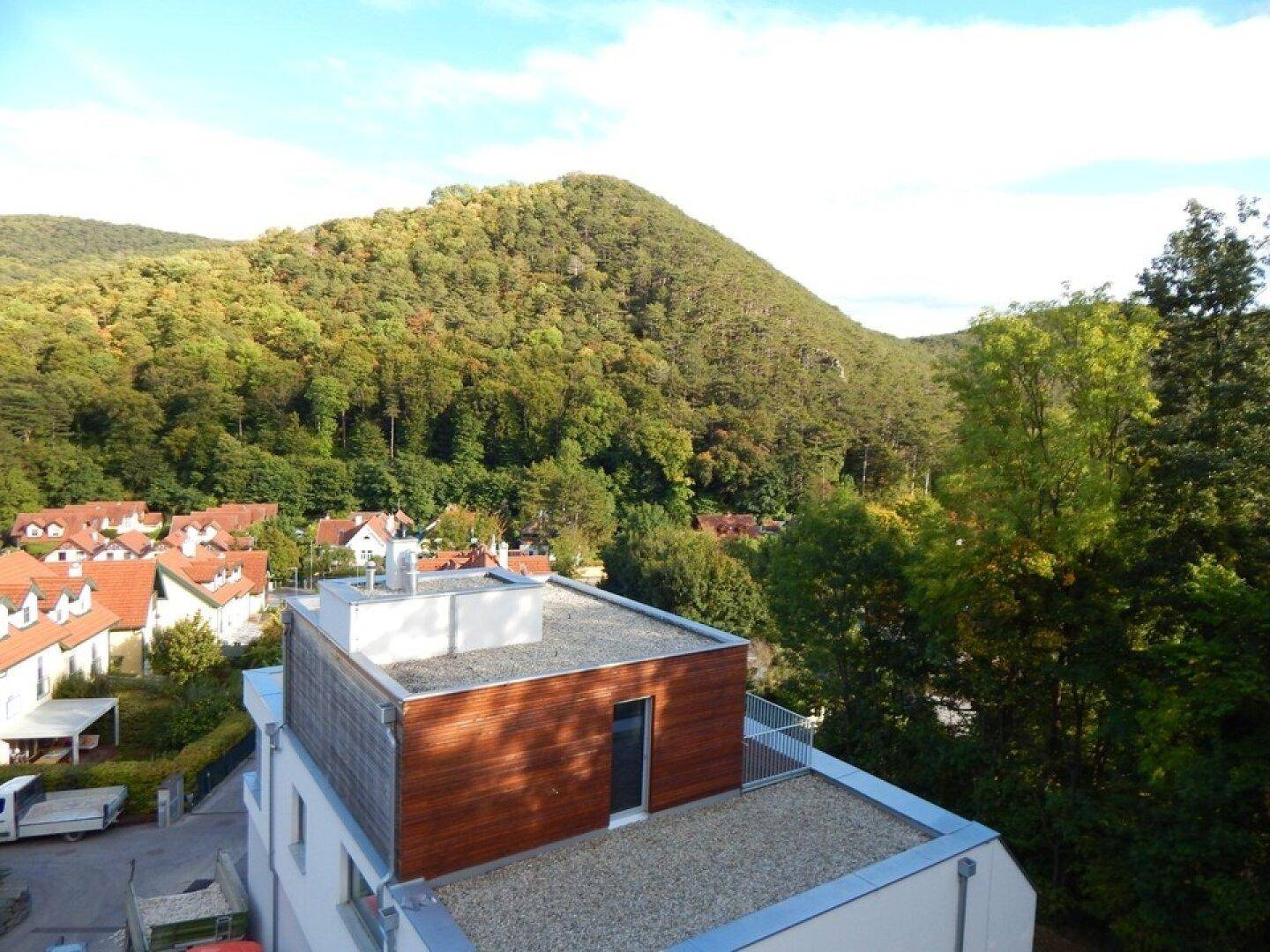 Dachansicht eines modernen Gebäudes mit Flachdach und Kiesbelag, umgeben von grünen Hügeln.