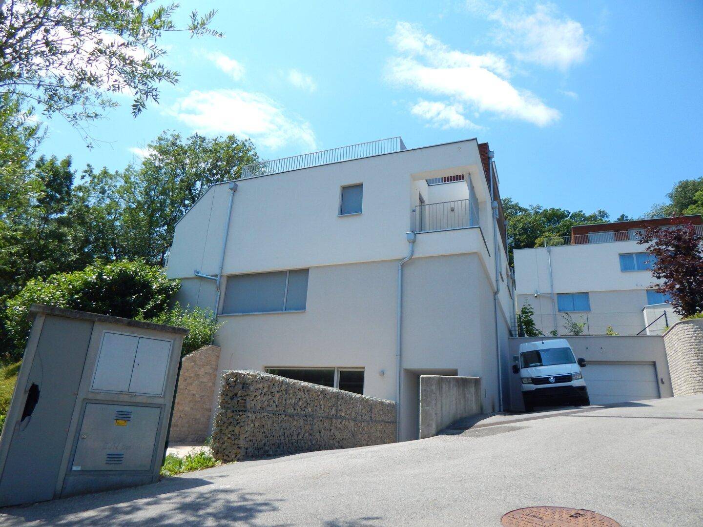 Moderne Villa mit weißer Fassade, Garagenzufahrt und umgebender grüner Landschaft.