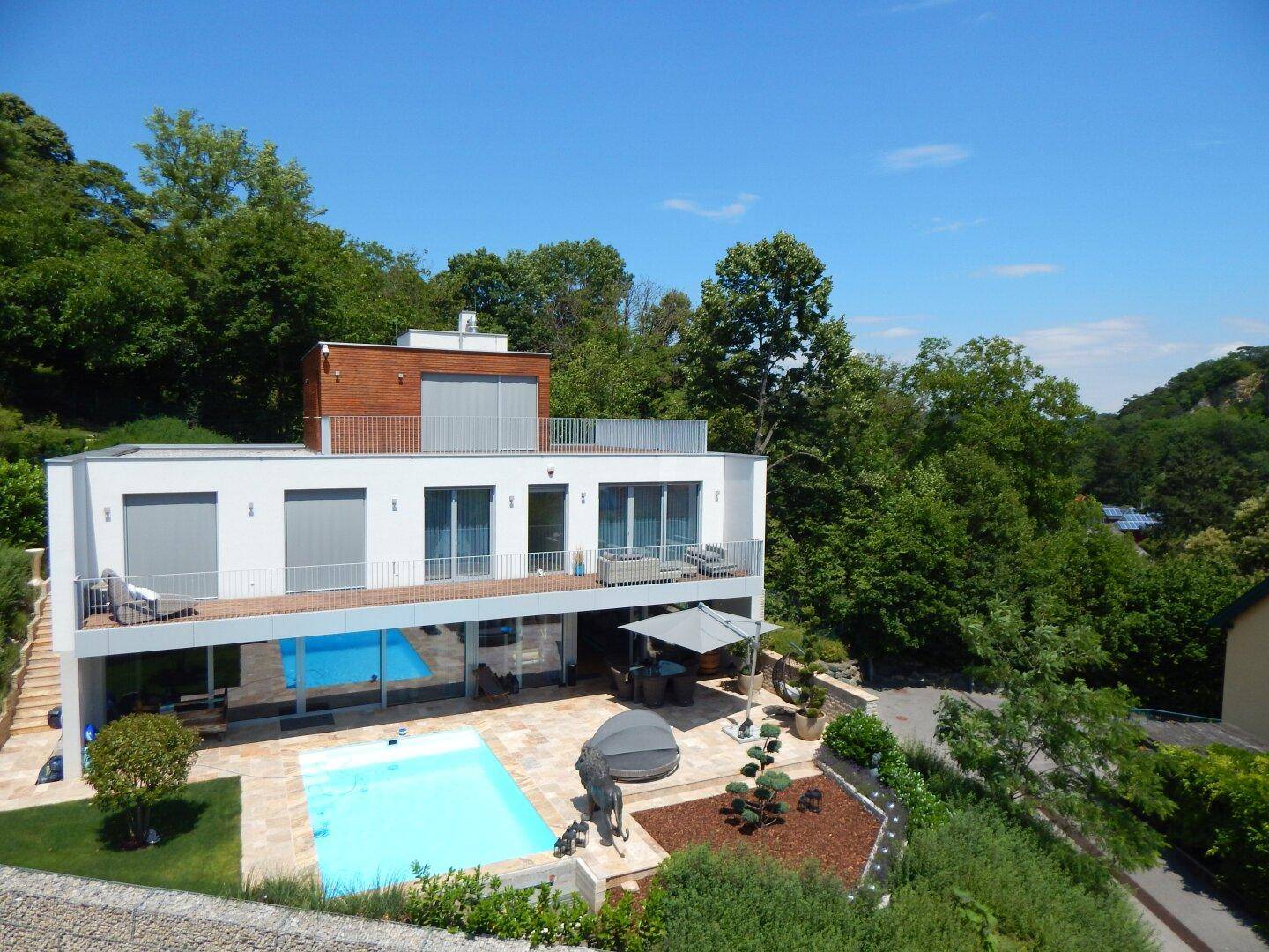 Moderne Villa mit mehreren Terrassen, Pool und gepflegtem Garten in grüner Hanglage.