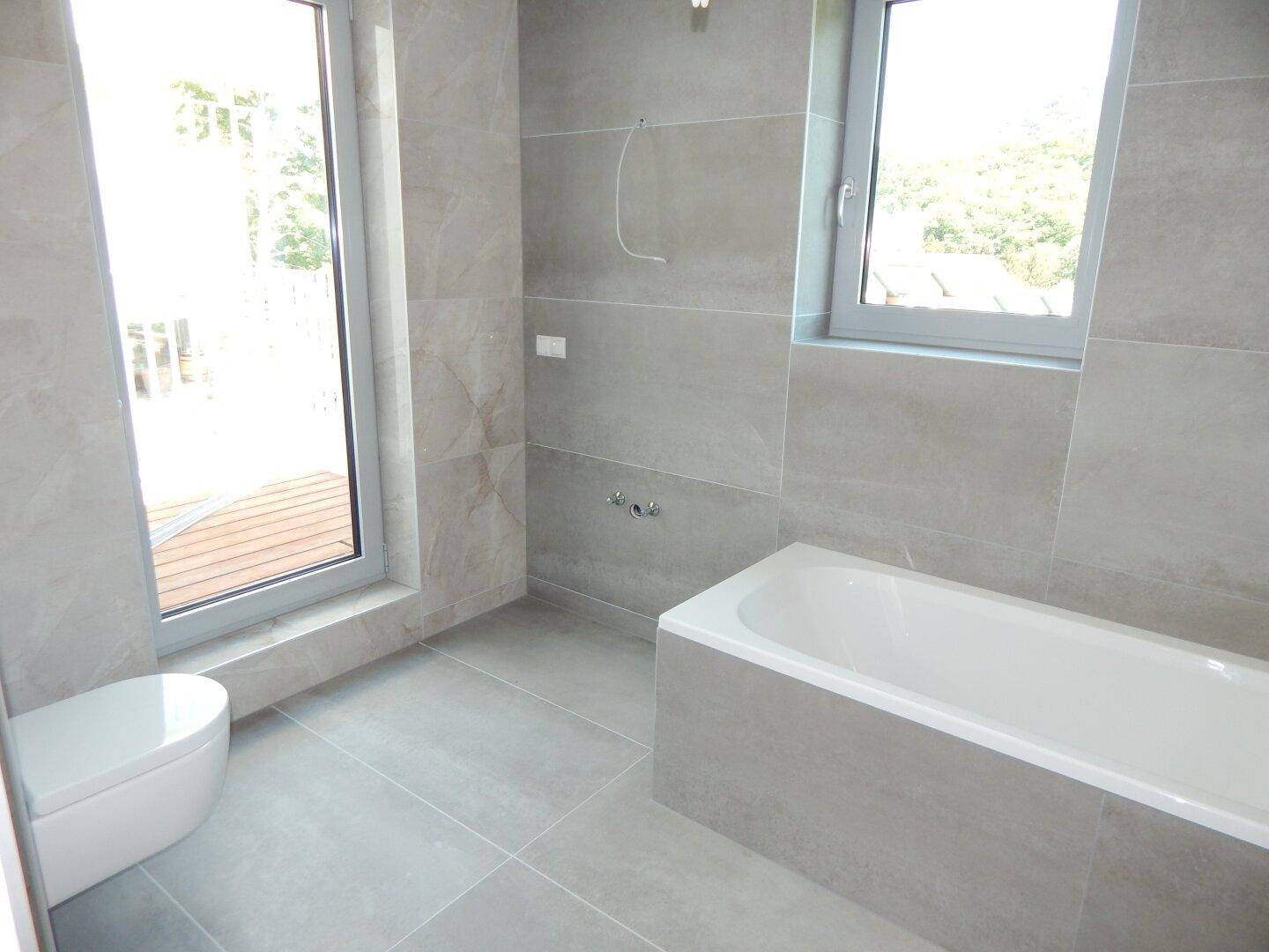 Modernes Badezimmer mit großen grauen Fliesen, Badewanne und wandhängendem WC.